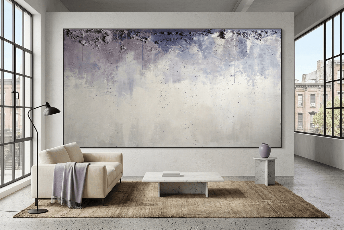 Overburden abstract artwork with a dark slate-violet plaster-like accumulation and fine drips above a chalk-white field with pale blue-grey veils in an industrial loft