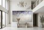 Overburden abstract artwork with a dark slate-violet plaster-like accumulation and fine drips above a chalk-white field with pale blue-grey veils in a two story foyer