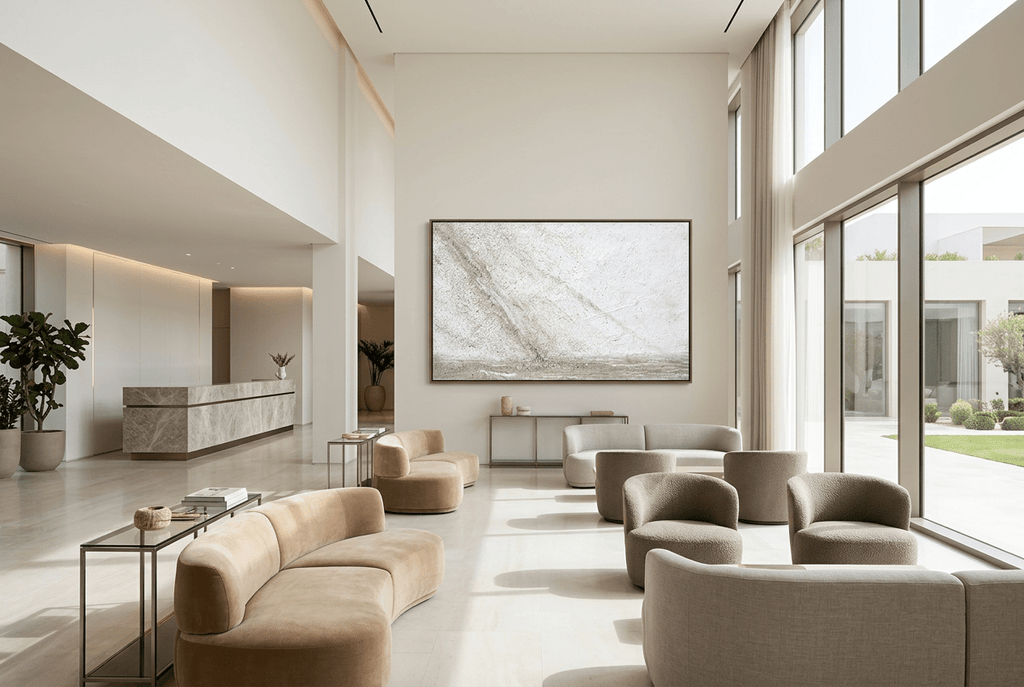 Unfilled Field abstract artwork with a pale cream and chalk-white textured field, a soft warm-grey diagonal drift, fine fissures, and a low stone-grey residue band in a modern hotel lobby