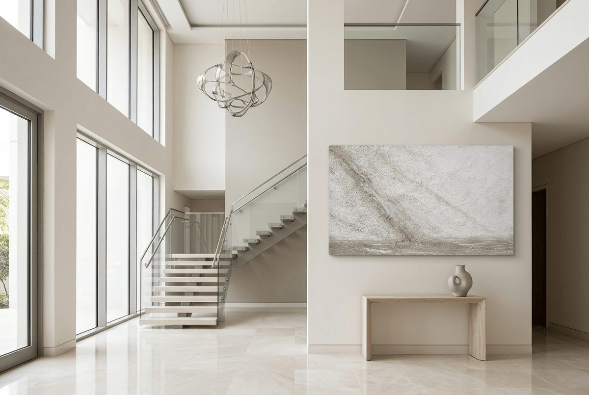 Unfilled Field abstract artwork with a pale cream and chalk-white textured field, a soft warm-grey diagonal drift, fine fissures, and a low stone-grey residue band in a two story foryer